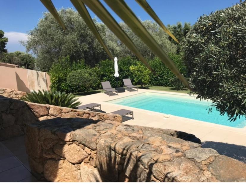 une piscine avec deux chaises et un mur en pierre dans l'établissement Villa Ysee, à Porto-Vecchio