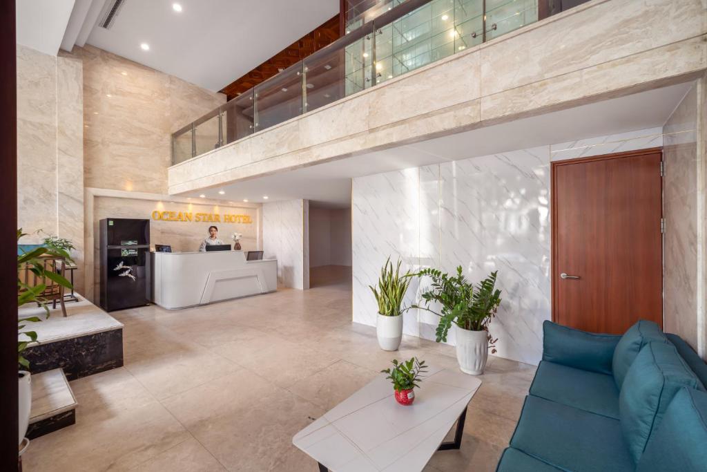 A bright hotel lobby with a reception desk, blue sofa, marble finishes, and indoor plants.