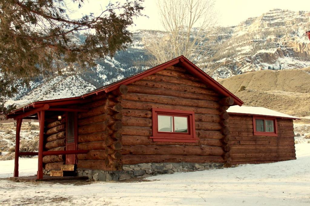 a log cabin with a red window in the snow at Family Cabin Rental on Beautiful Ranch near Yellowstone National Park, Wyoming in Wapiti