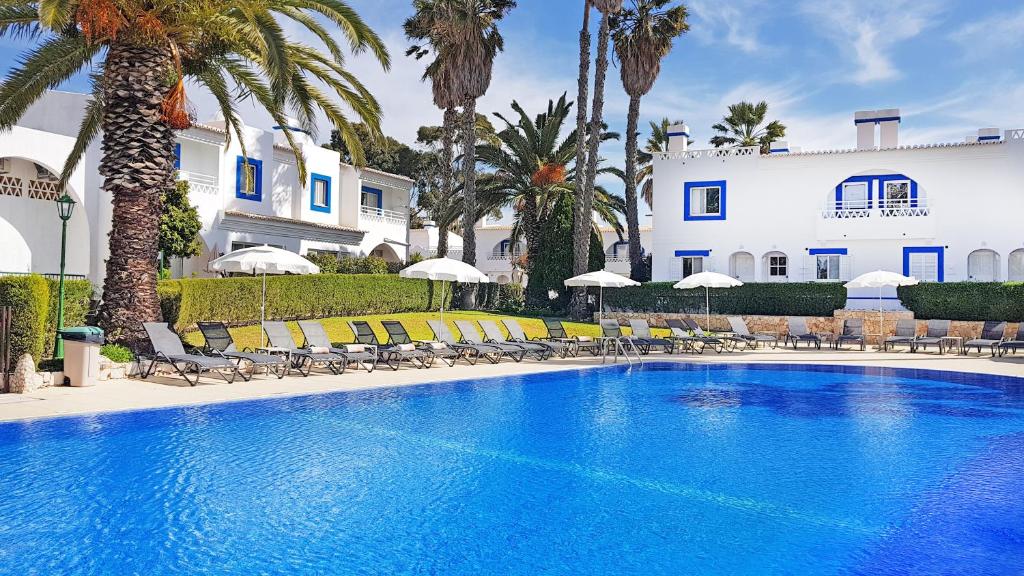 a pool with chairs and palm trees in front of a building at Pestana Palm Gardens in Carvoeiro