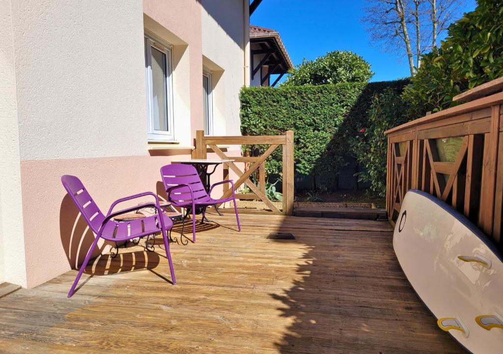 une terrasse avec des chaises violettes, une table et une planche de surf dans l'établissement LILAS - Appartement pour 4 à proximité des commerces, à Capbreton