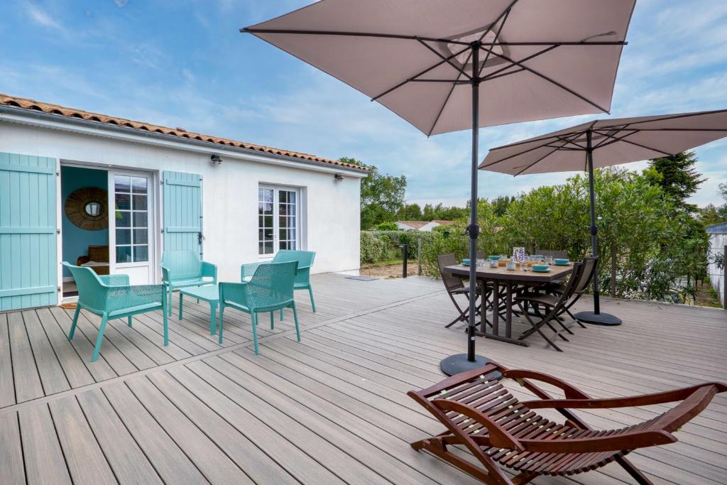 una terraza de madera con mesa, sillas y sombrilla en Maison des Bouillats - Welkeys, en Saint-Trojan-les-Bains
