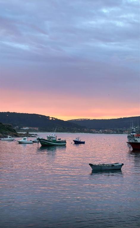 a group of boats sitting in the water at sunset at Cruz de Baixar in Fisterra