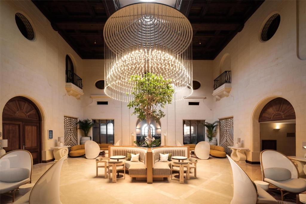 a large lobby with a large chandelier and tables and chairs at Kempinski Hotel San Lawrenz in San Lawrenz