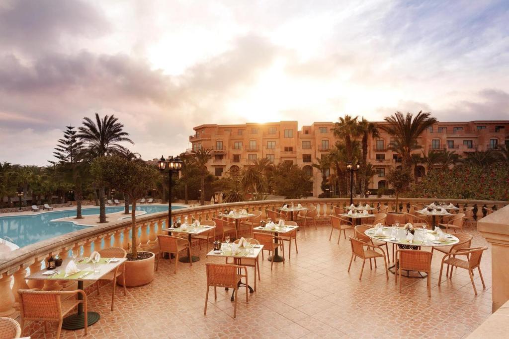 a restaurant with tables and chairs next to a pool at Kempinski Hotel San Lawrenz in San Lawrenz