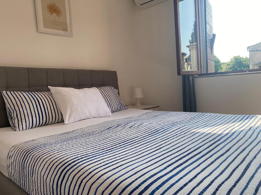 a bed with a blue and white striped comforter and a window at Guest House Marta in Rovinj