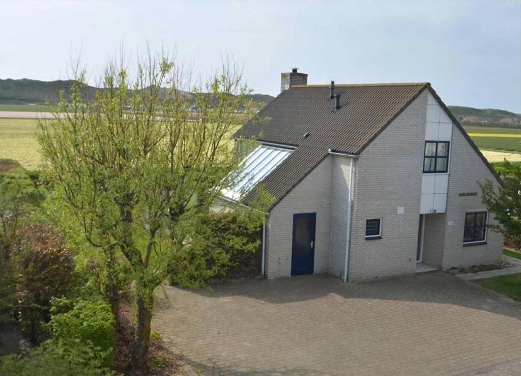 een wit huis met een blauwe deur en een boom bij Luxusvilla Ooghduyne Mit Privatem Whirlpool in Julianadorp