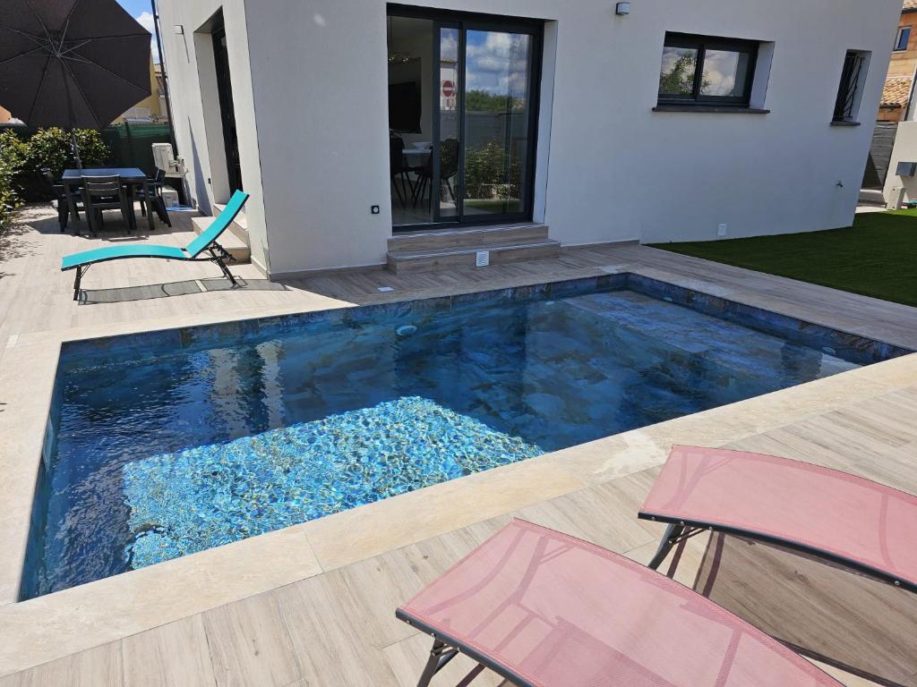 une piscine avec deux chaises et une maison dans l'établissement Villa neuve avec piscine, à Vauvert