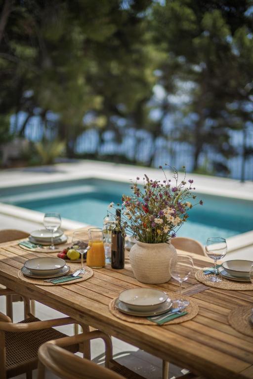 a wooden table with plates and glasses and a vase of flowers at Villa Vartal in Ivan Dolac