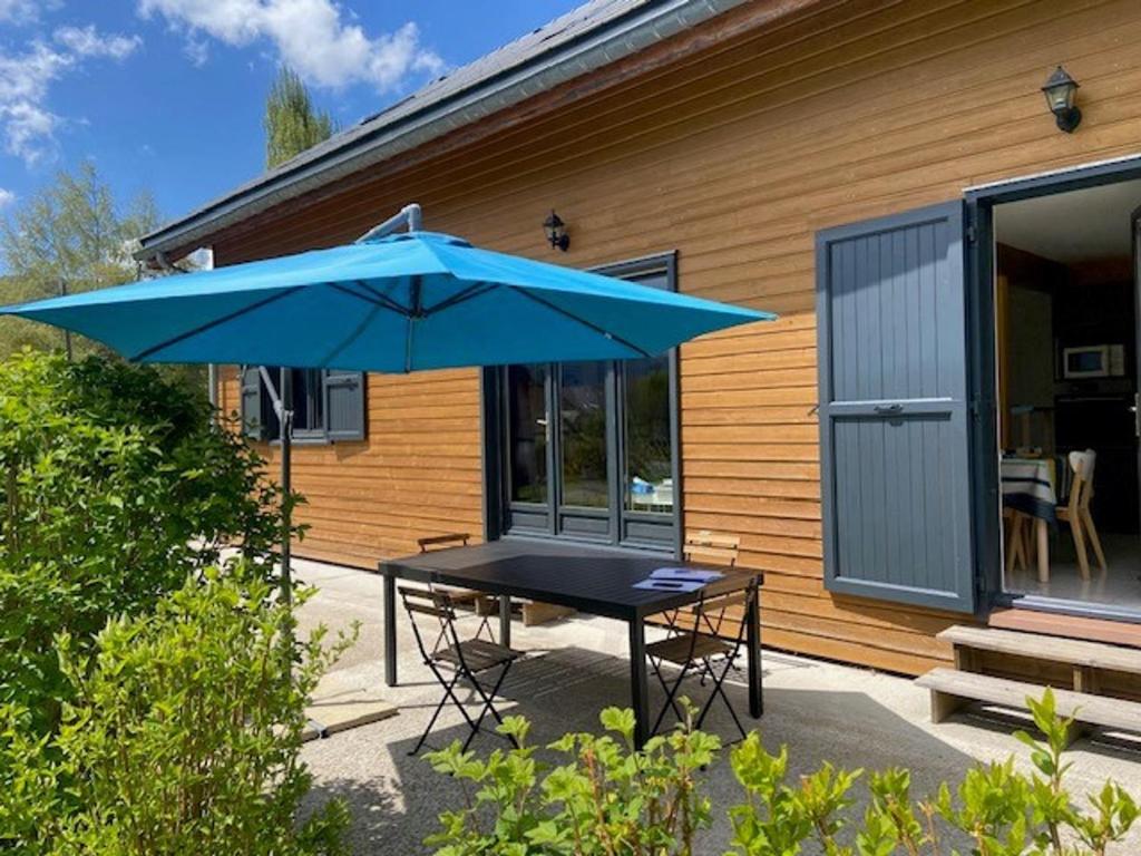 une table avec un parapluie bleu devant une maison dans l'établissement Belle Maison à Autrans, 4 Chambres, 8 Pers, Jardin, Proche Village et Pistes de Ski - FR-1-737-14, à Autrans