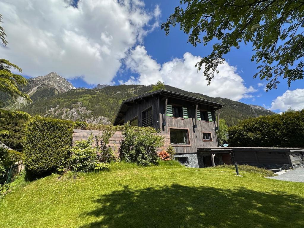 une maison sur une colline herbeuse avec des montagnes en arrière-plan dans l'établissement Chalet 8 Etoiles, à Chamonix-Mont-Blanc