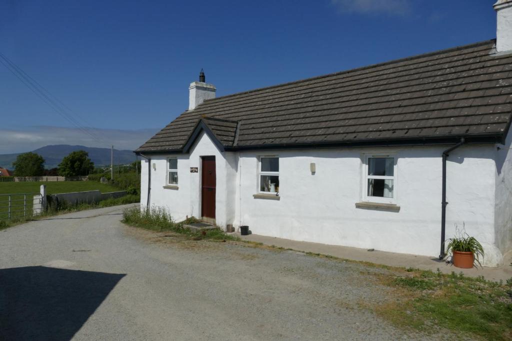 une maison blanche avec un toit noir sur une route dans l'établissement Carol Cottage, à Kilkeel