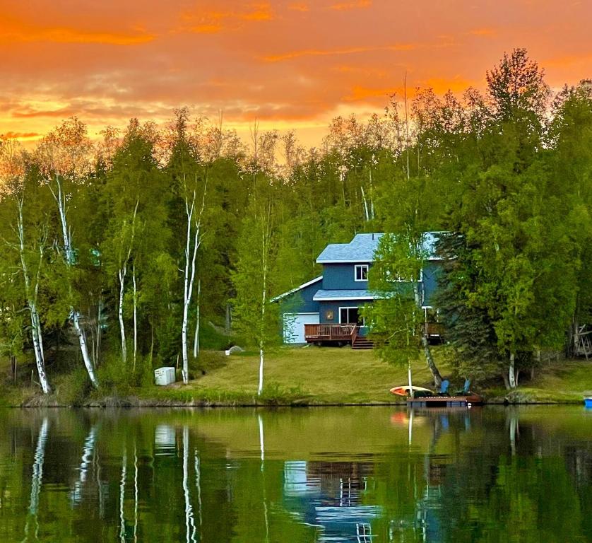 a house on the shore of a lake at sunset at Serene Four Bedroom Lakefront Home in Wasilla