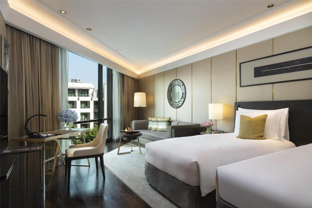 A bright guest room with two beds, a window-side desk and a separate seating area.