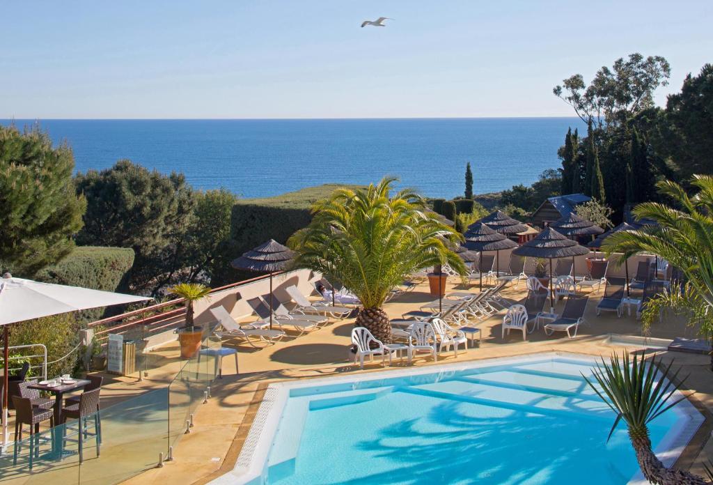 a resort with a swimming pool with chairs and umbrellas at Hôtel & Spa Les Mouettes in Argelès-sur-Mer
