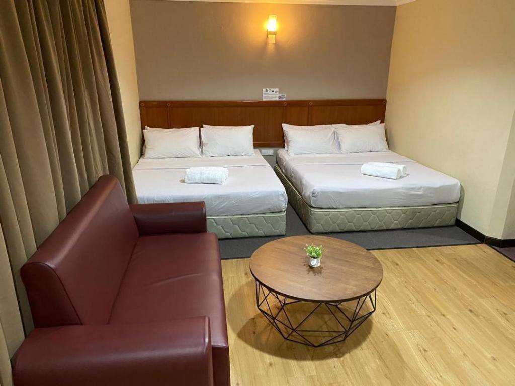 a room with two beds and a couch and a table at Hotel Perdana in Lawas