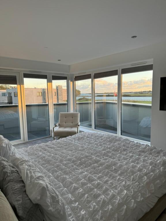 a bedroom with a bed and a chair and windows at Modern 5 Bedroom Luxury Home with Sea Views and Hot Tub in North Hayling