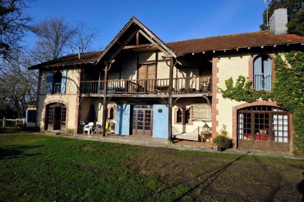 une grande maison en briques avec une terrasse dans une cour dans l'établissement ecurie de bidalon, à La Celle-sous-Gouzon