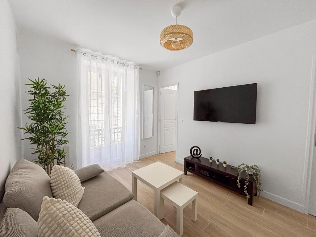a living room with a couch and a tv on a wall at Appartement lumineux et moderne, proche transports in Pantin