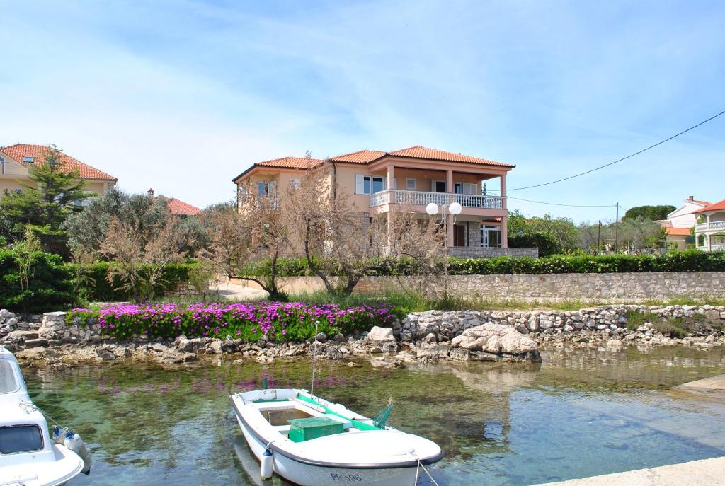 a boat in the water in front of a house at Apartmani Villa Dragica in Ugljan