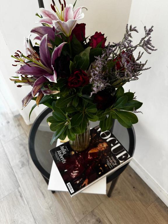 un jarrón de flores en una mesa con una revista en Luxury Olive Haven 1Bed, 1 Min to DLR & University, en North Woolwich