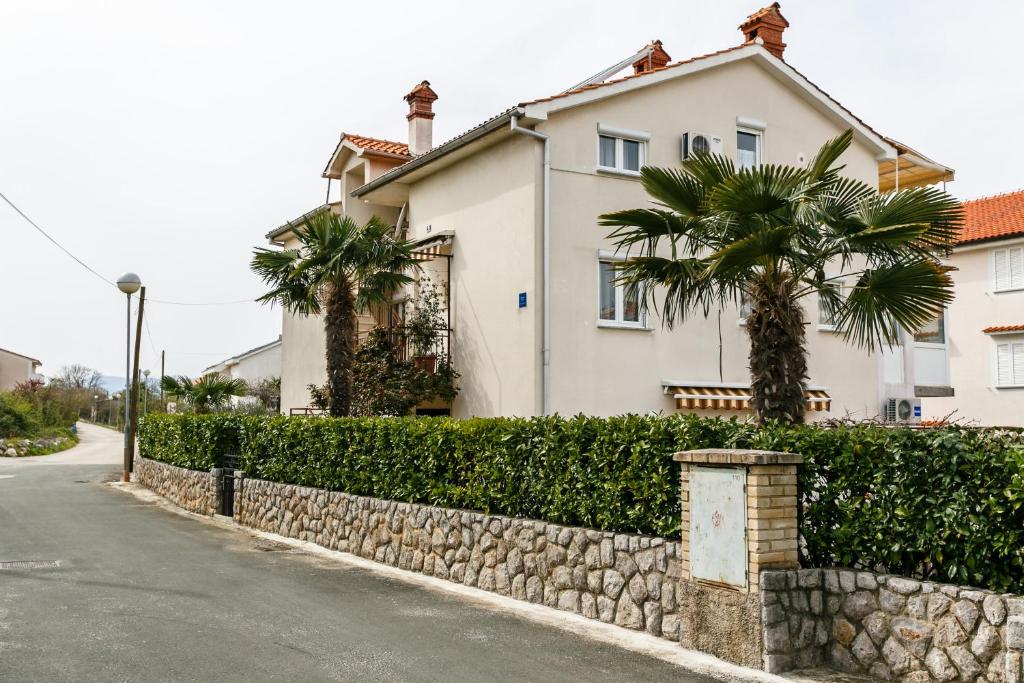 ein weißes Haus mit Palmen und einer Steinmauer in der Unterkunft Apartmani Cvelic in Malinska