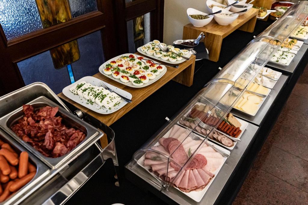 Breakfast buffet displaying sliced cold cuts, deviled eggs, bacon and sausages under serving covers.