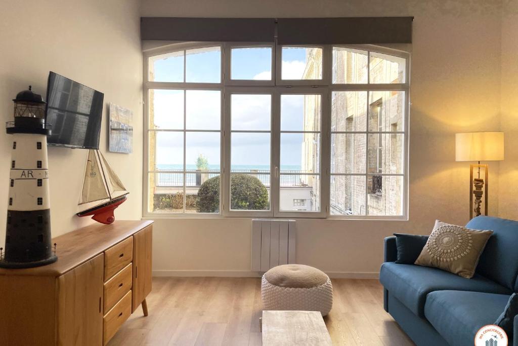 un salon avec un canapé bleu et une grande fenêtre dans l'établissement Le Sunset - Vue Mer - Accès plage privé, à Trouville-sur-Mer
