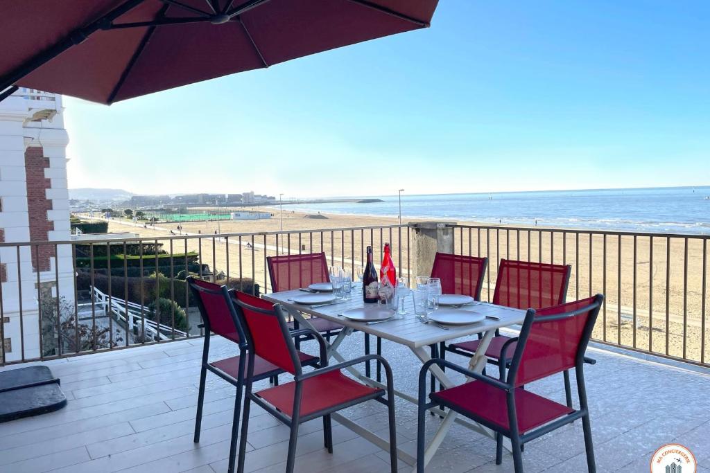 une table et des chaises sur un balcon avec l'océan dans l'établissement Les Roches Noires - Terrasse Vue Mer, à Trouville-sur-Mer