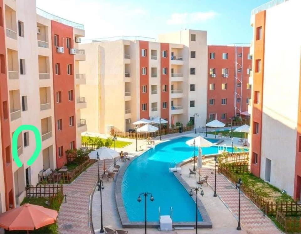 ein Pool mit Sonnenschirmen und einige Gebäude in der Unterkunft وحدة للإيجار في إحدى قرى الساحل الشمالي المميزة in Dawwār Abū Maḩrūs