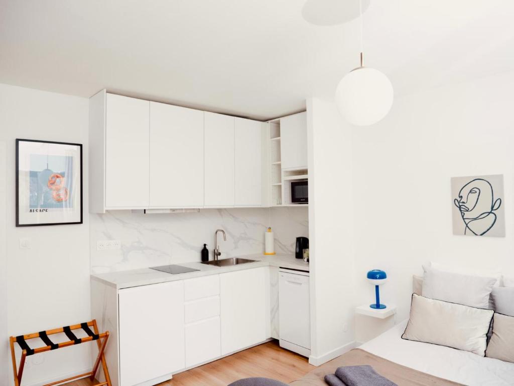 a white kitchen with white cabinets and a couch at Le signature - Magnifique Studio tout confort au coeur de Strasbourg in Strasbourg