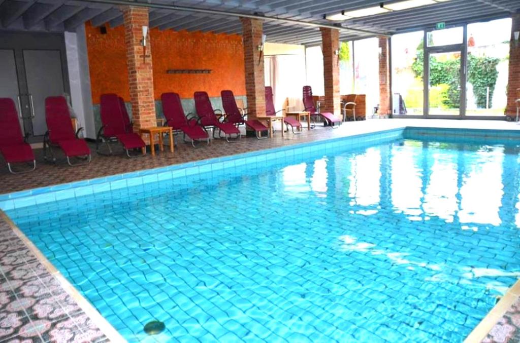 uma grande piscina com cadeiras vermelhas e cadeiras em Ringhotel Alpenhof - Patchworkhotel em Augsburg
