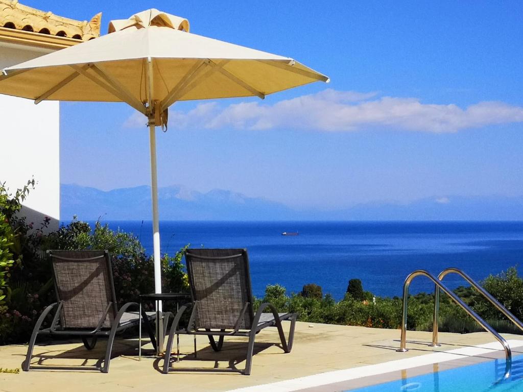 two chairs and an umbrella next to a swimming pool at The Iconpainter Peroulia Villa in Kómboi