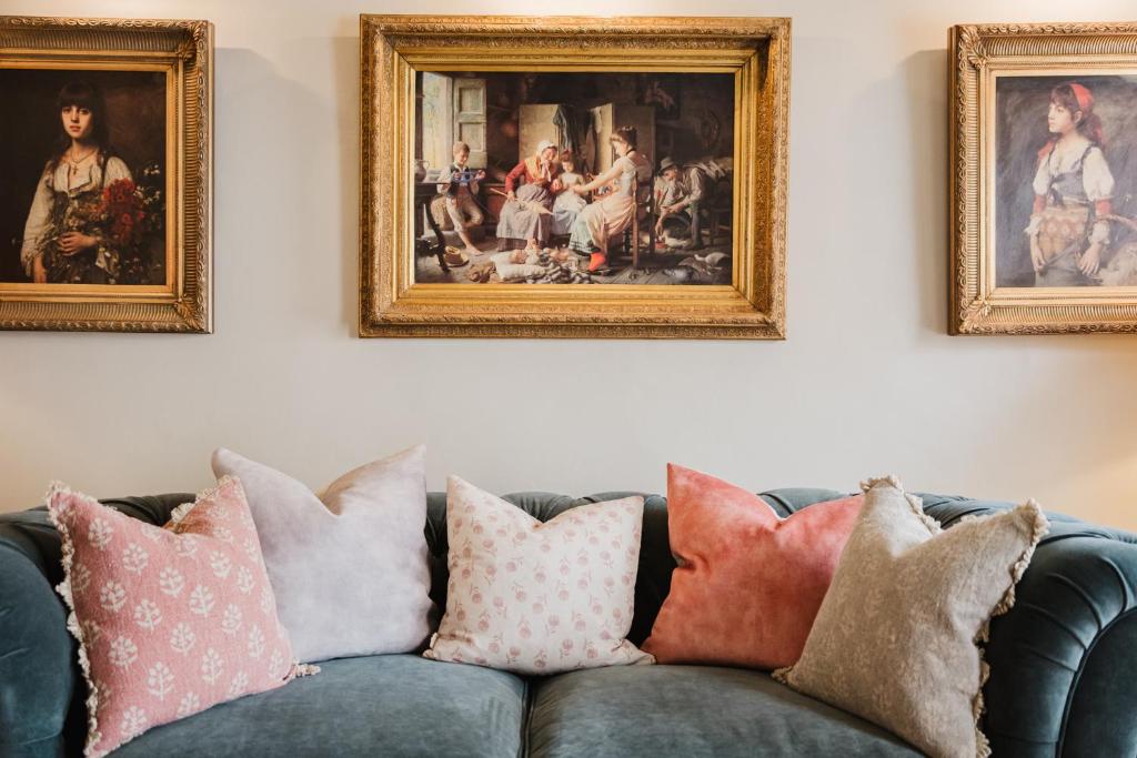 ein Sofa mit Kissen in einem Wohnzimmer mit Gemälden in der Unterkunft Hicks House - Beautiful Cottage in Leysbourne! in Chipping Campden