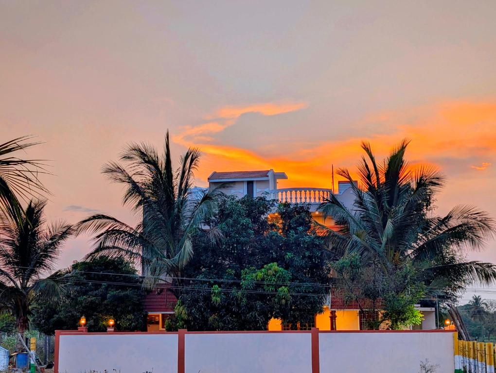 a building with palm trees in front of a sunset at Yellowra Farmstay Tiruvannamalai in Tiruvannāmalai
