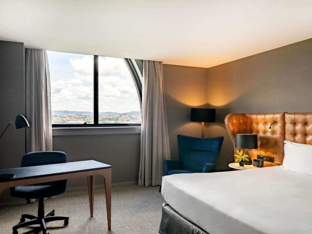 a hotel room with a bed and a desk and a window at Pullman Sao Paulo Guarulhos Airport in Guarulhos