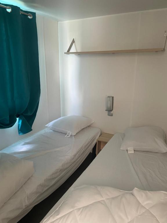 two beds in a room with a blue curtain at Mobilhome in Litteau