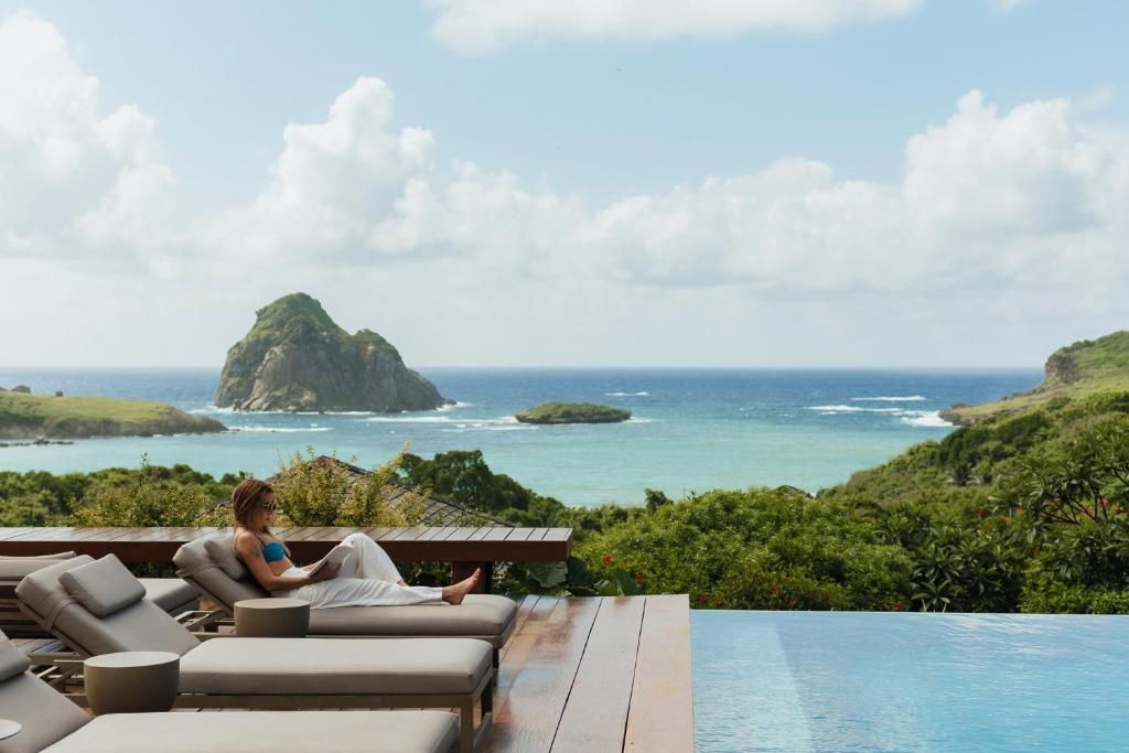 a woman sitting on a couch next to a swimming pool at Pousada Maravilha in Fernando de Noronha