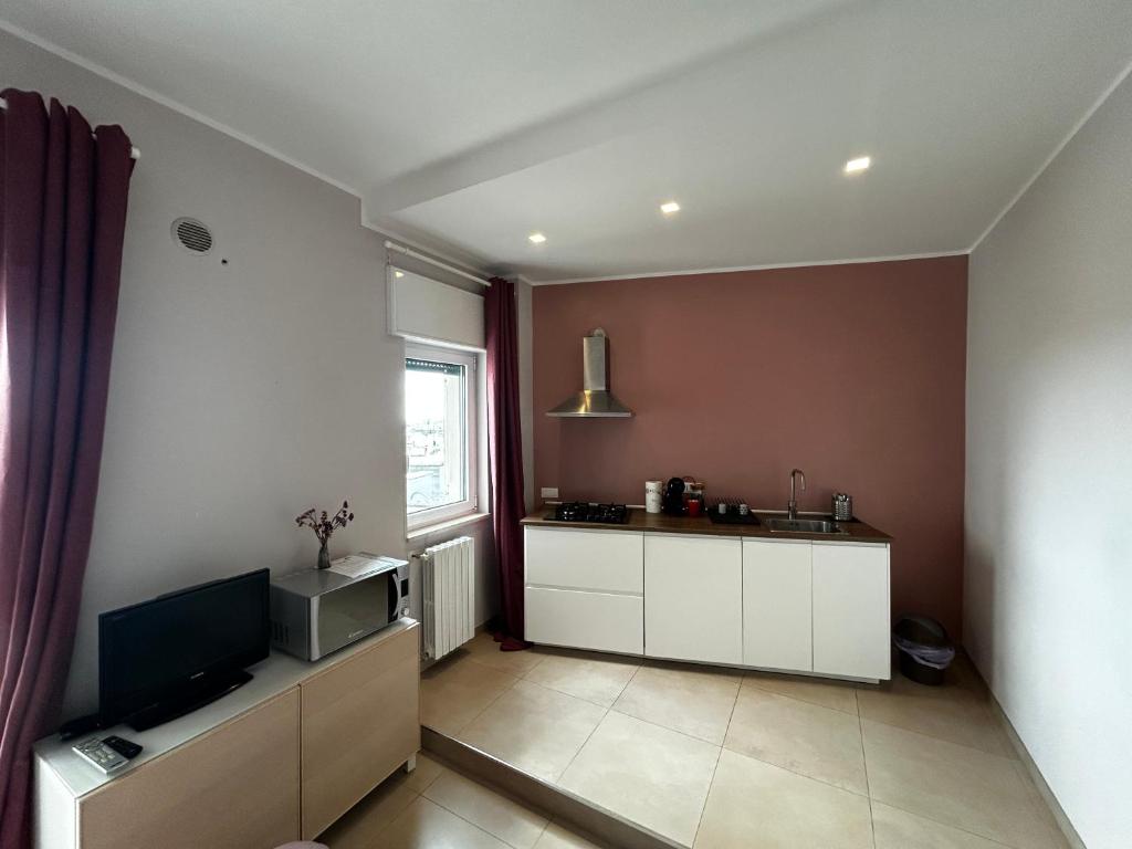 kuchnia z białymi szafkami, telewizorem i oknem w obiekcie Apartment Antonella w mieście Ostuni