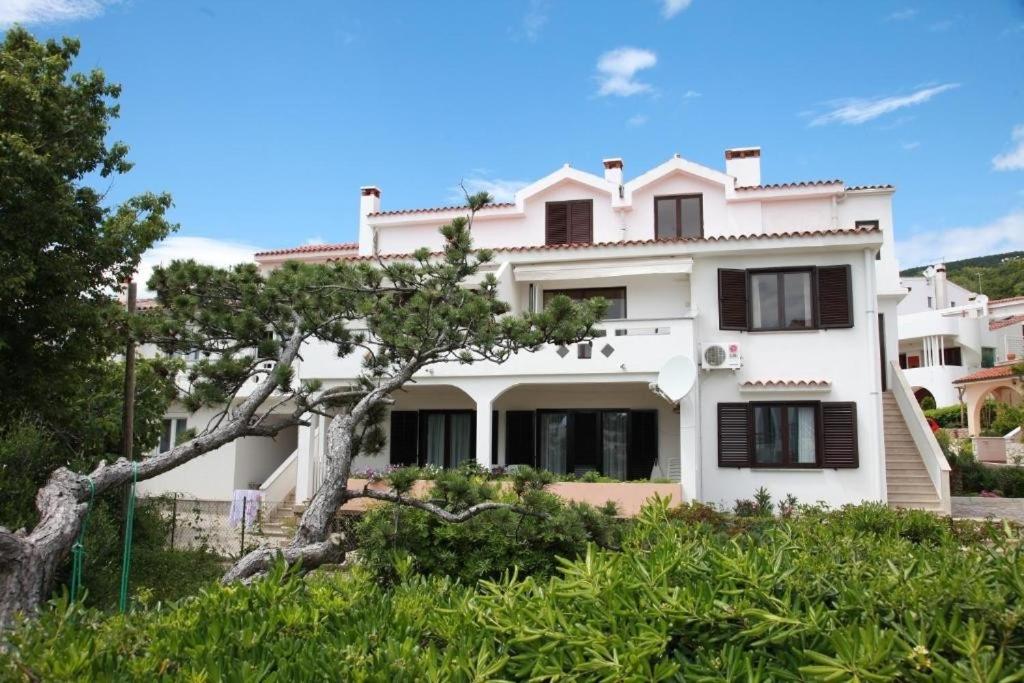 una casa blanca con un árbol delante en Apartments by the sea Baska, Krk - 24433, en Baška