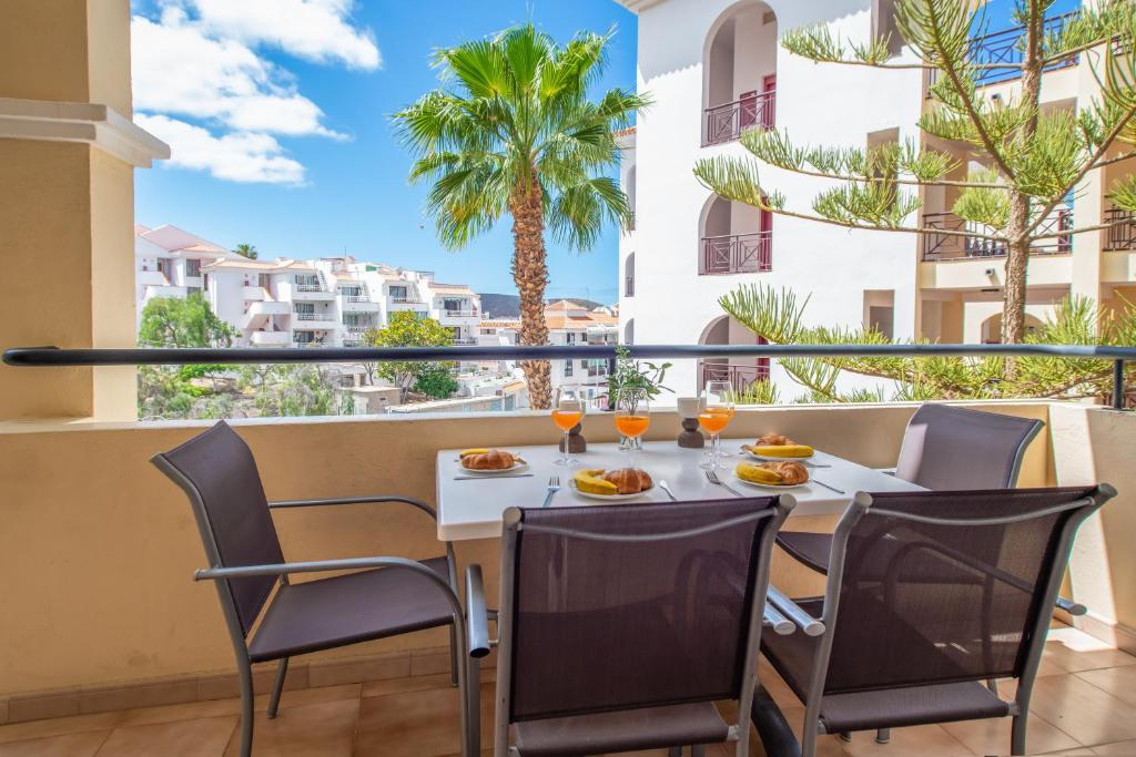 a table with food and drinks on a balcony with palm trees at Castle Harbour with heated pool ap Patricia in Los Cristianos