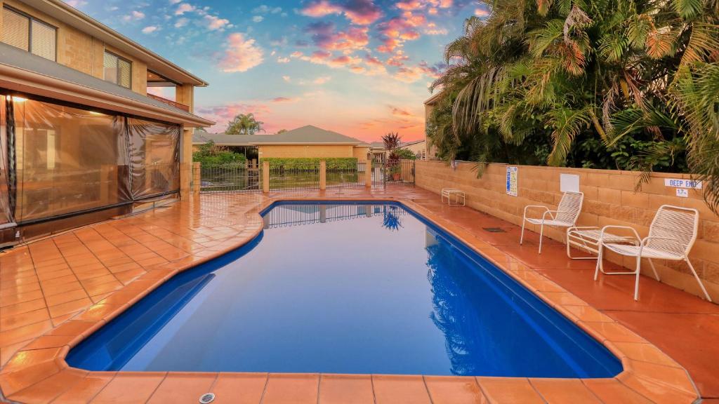 a swimming pool with chairs and a house at Emerald Gardens Motel & Apartments in Emerald