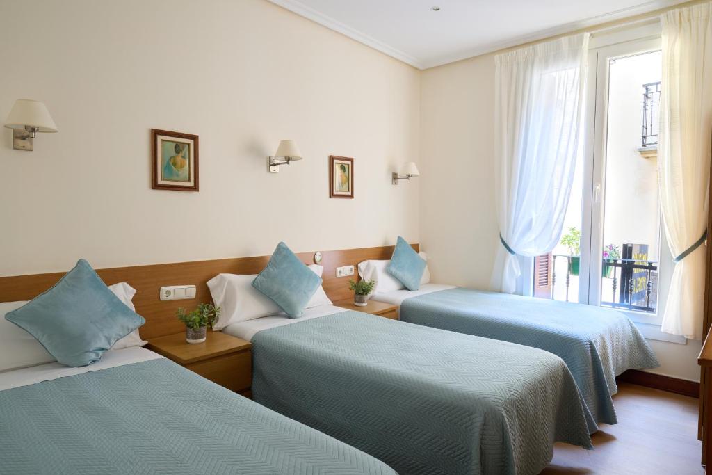 una habitación con tres camas y una ventana en Pensión San Jerónimo, en San Sebastián