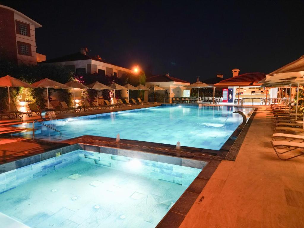 a large swimming pool at night with chairs and umbrellas at Kamer Exclusive Hotel & Suites in Çeşme