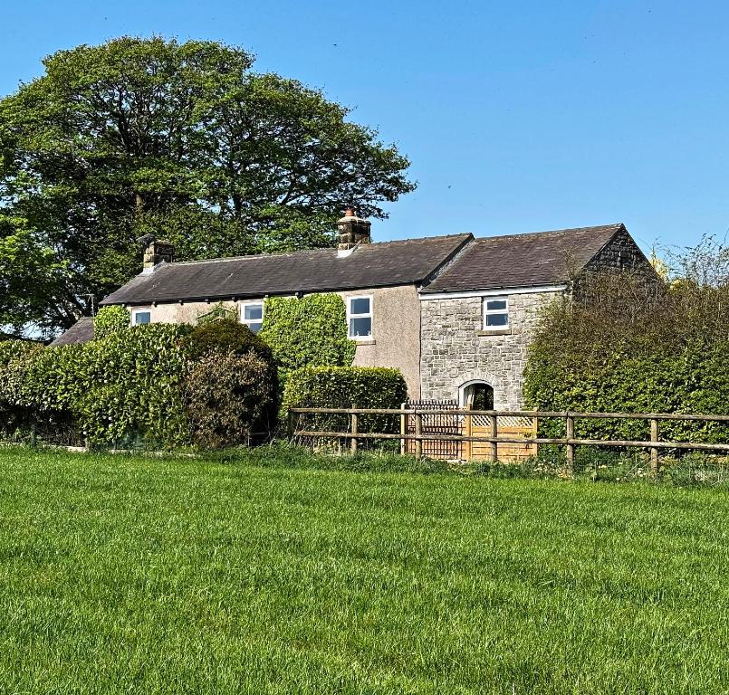 a stone house with a fence in a field at Bruntmoor Cottage in Bakewell