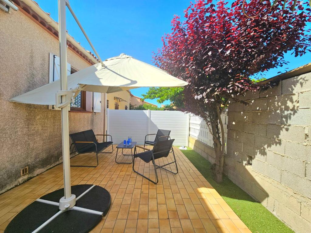 un patio avec un parasol, des chaises et une table dans l'établissement Grande maison familiale proche plage Barcarès, au Barcarès