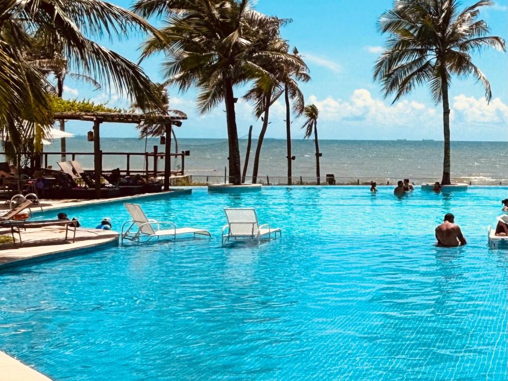 a large swimming pool with palm trees and the ocean at Condomínio Wai Wai Pé na Areia - Praia de Cumbuco in Cumbuco
