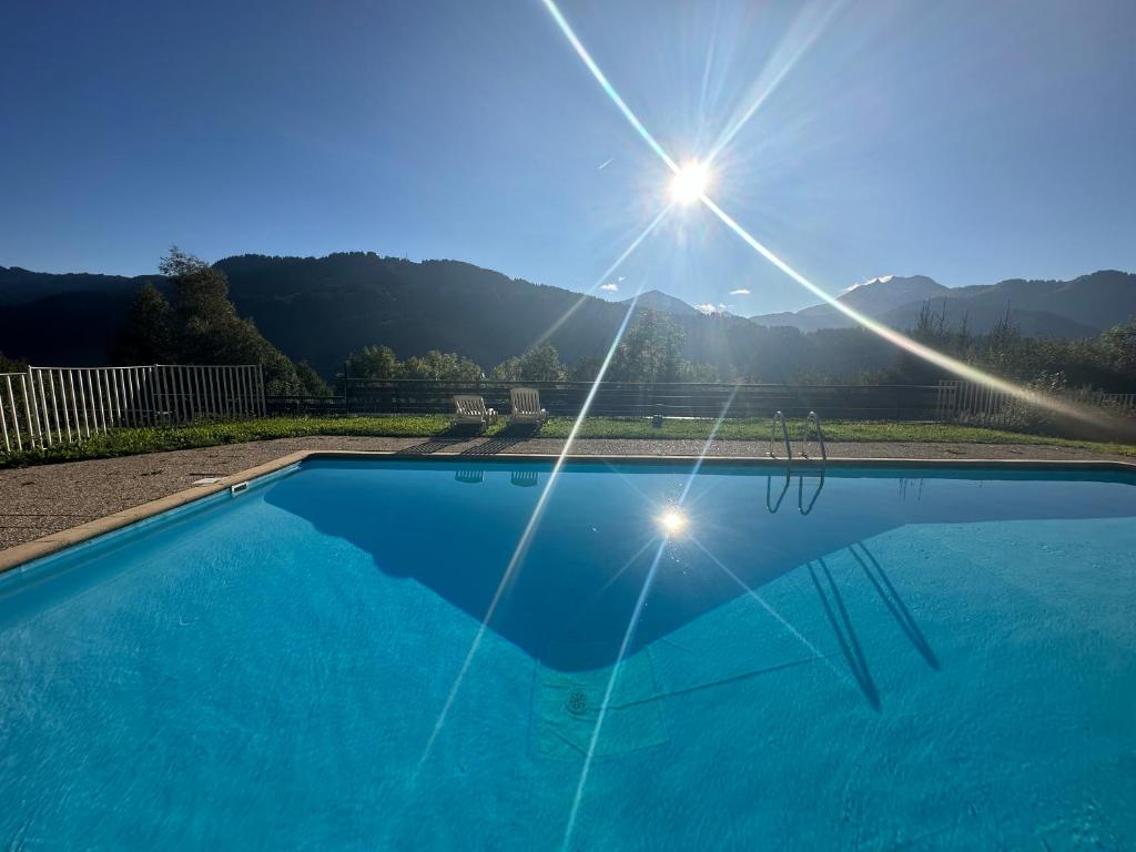 a blue swimming pool with the sun in the sky at charmant studio à Morzine avec piscine privé in Morzine