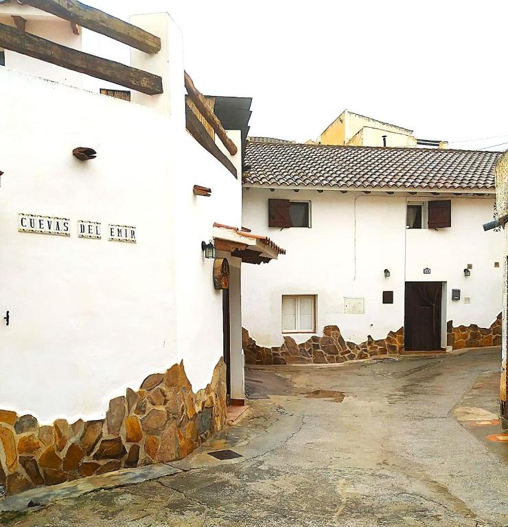 a white building with a stone wall and a door at Casa Cueva, Cuevas del Emir in Freila