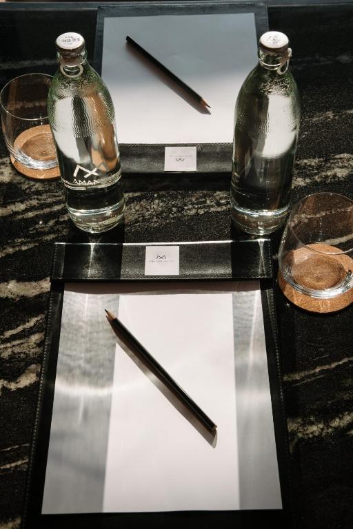 A tabletop writing setup includes bottled water, glasses, notepads, and pencils.